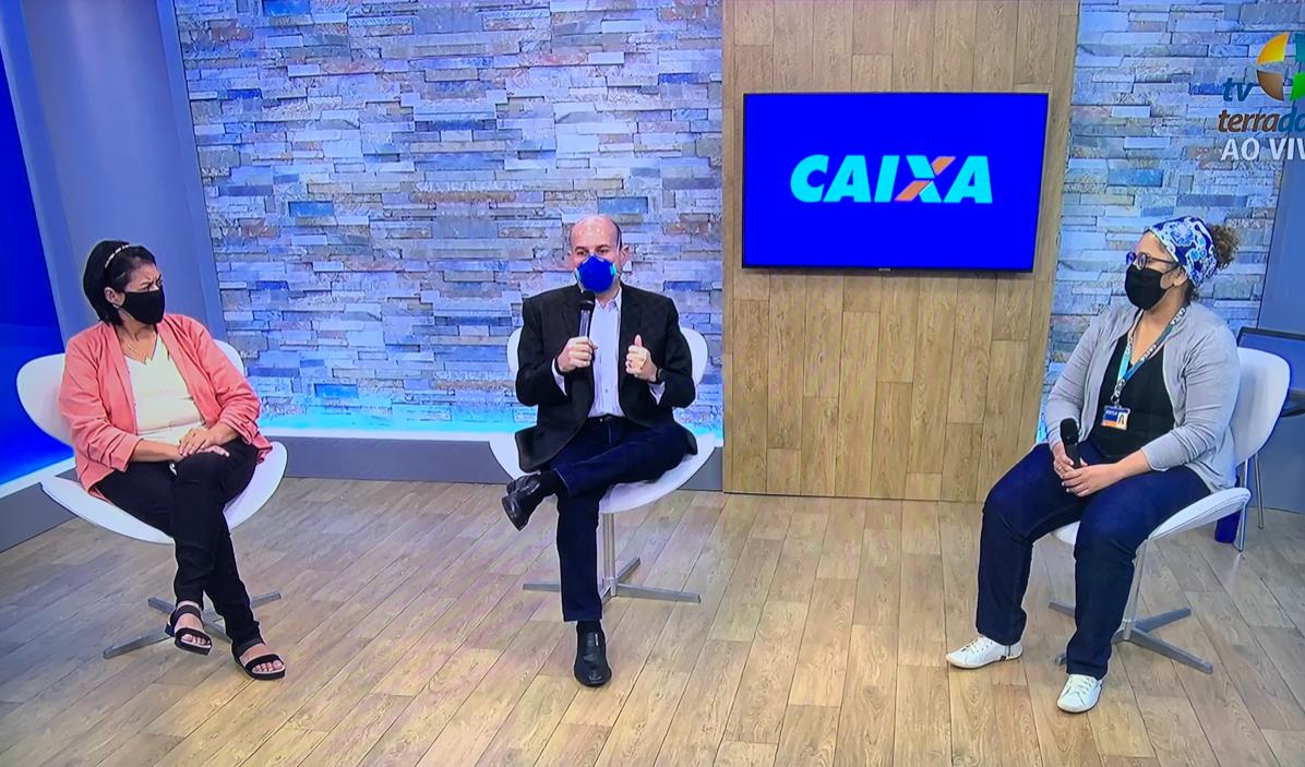 prefeito e duas senhores sentados em cadeiras em estúdio de TV todos usando máscara